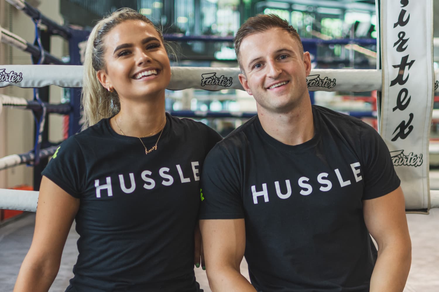 Two employees wearing Hussle t-shirts, side by side smiling at the camera.